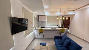 A modern living room with a blue sofa, a round coffee table, and a flat-screen TV mounted on the wall.