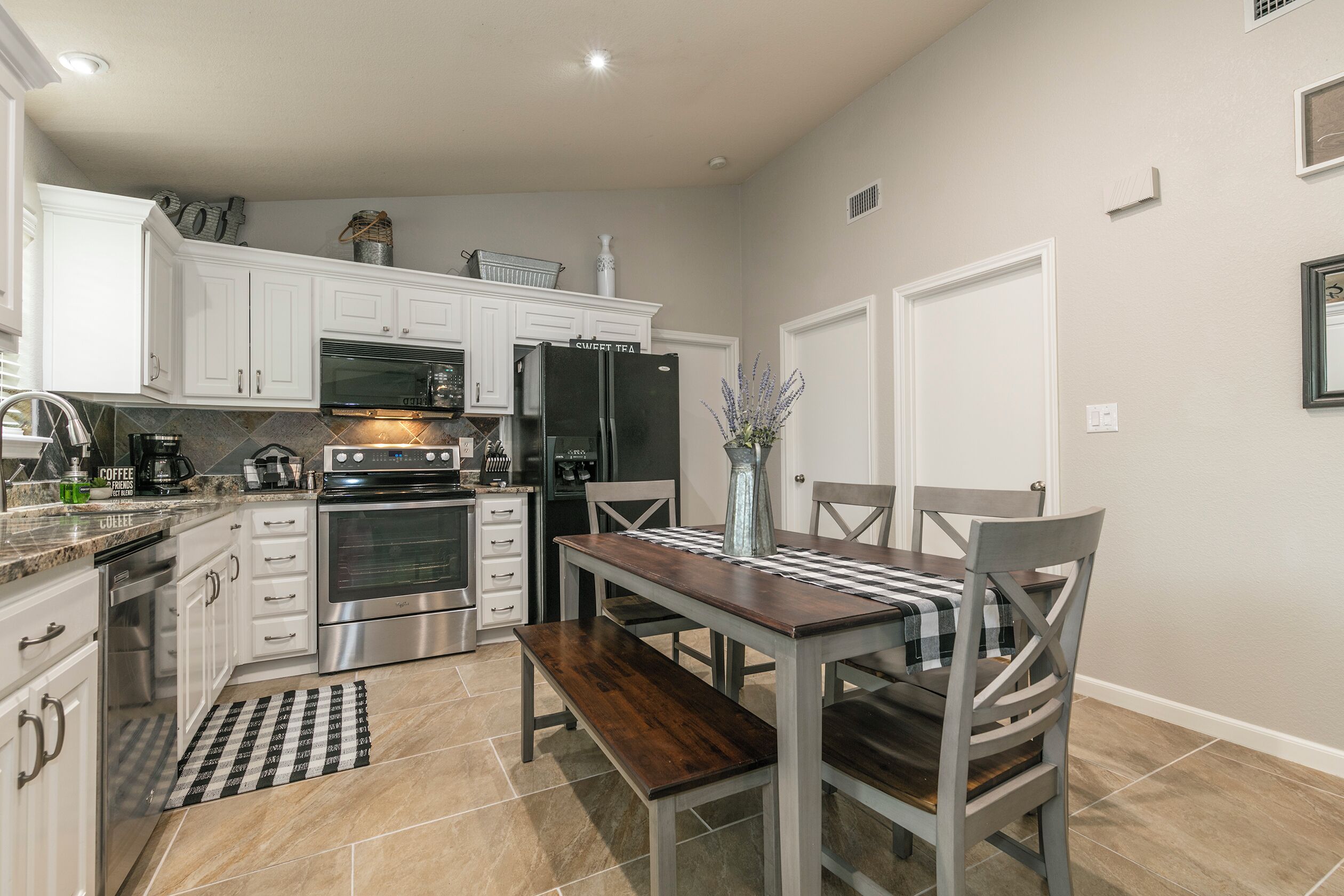 Una cocina moderna con armarios blancos, electrodomésticos de acero inoxidable y un comedor con mesa y sillas de madera.