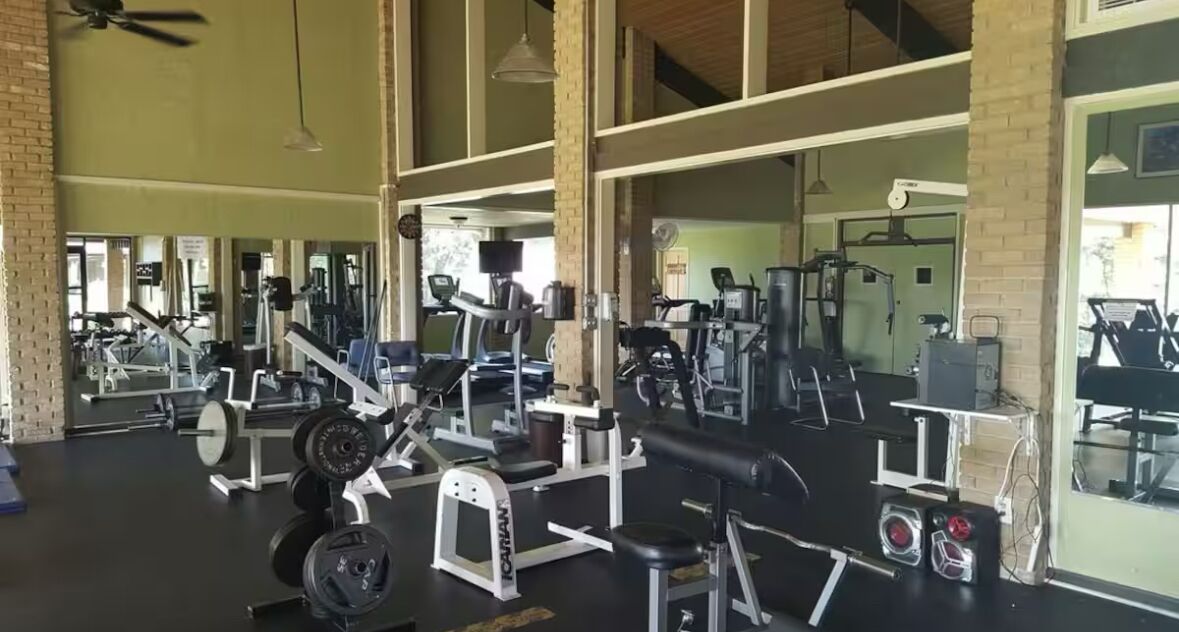 A gym with various exercise equipment, large windows, and a high ceiling.