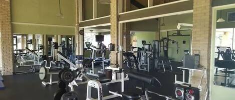 A gym with various exercise equipment, large windows, and a high ceiling.