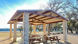 A covered picnic area with stone pillars and wooden benches, surrounded by trees and a view of the landscape. - Lake Travis Retreat! Kayaks/Boat Launch/Pool/Park/Point Venture/"Summit Ridge" (Lago Vista)