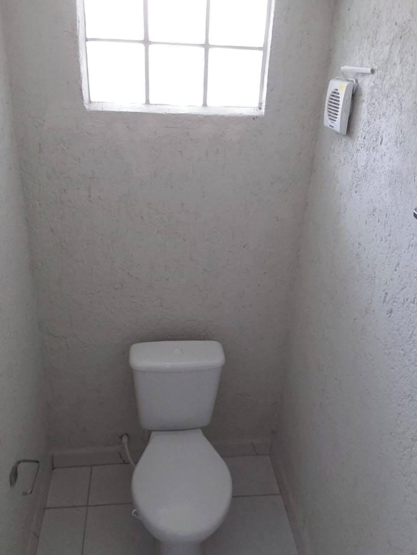 Une petite salle de bain blanche, équipée de toilettes, d’une fenêtre et d’un radiateur fixé au mur.