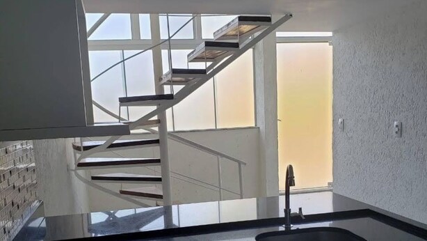 A modern kitchen with a gas stove, a sink, and a staircase leading to an upper level.