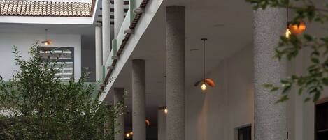 A corridor with large columns, potted plants, and a checkered floor pattern.