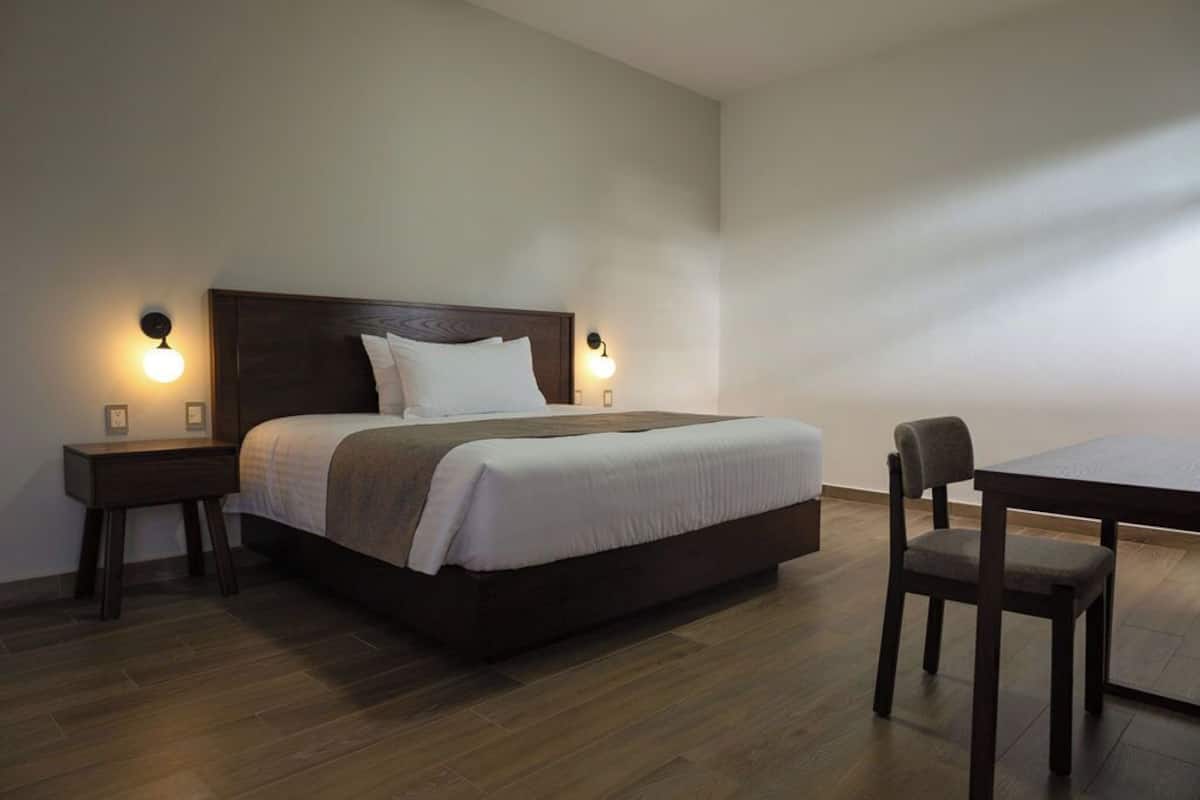 Un dormitorio con una cama grande, dos mesitas de noche, una silla y una pequeña mesa.