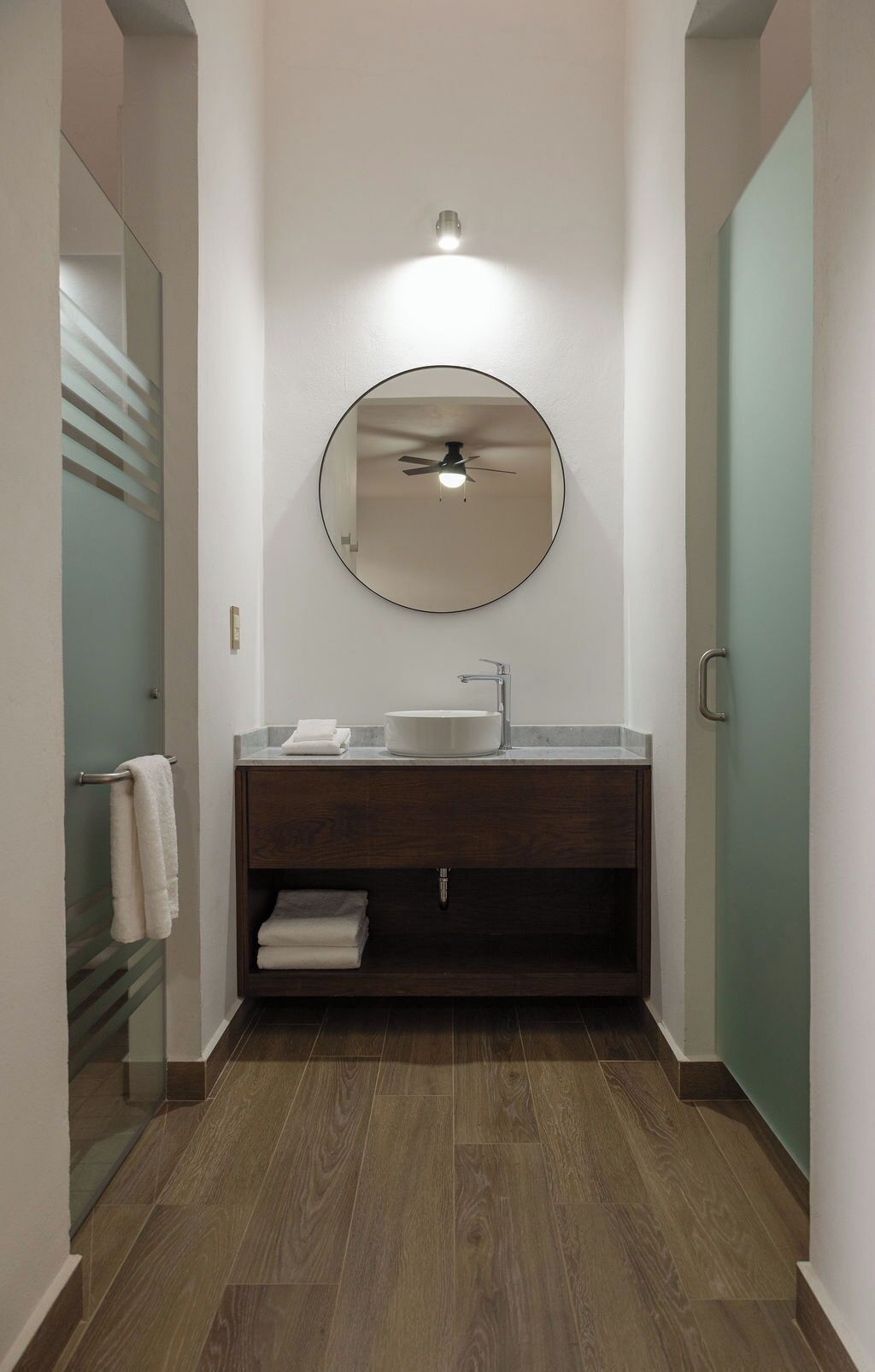 Un baño moderno con un espejo redondo, un lavamanos y un ventilador de techo.
