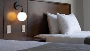 Una camera d'albergo con una testiera in legno, una lampada da comodino e un letto con biancheria bianca.