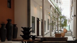 Un'ampia area interna con soffitto alto, ampie finestre e una scala che conduce a un livello superiore. In primo piano, diverse grandi vasi e una panca.