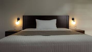 Una cama bien tendida con una almohada blanca y una manta marrón, flanqueada por dos mesitas de noche con lámparas de pared.