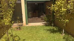 Un patio con una verja verde, un árbol pequeño y una zona con césped.