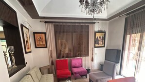 Una sala de estar con un sofá, sillones, una mesa de centro de vidrio, una araña y un televisor.