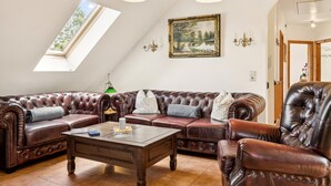 A spacious living room with a large L-shaped brown leather sofa, a wooden coffee table, and a painting of a landscape on the wall. - Stunning home in Kenz Küstrow (Kenz Küstrow)