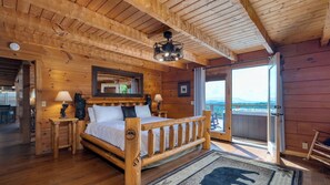 A wooden cabin bedroom with a bed, bedside lamps, a mirror, and a view through a glass door. - Big Bear Lodge by Avantstay Smoky Mountain Views, Hot Tub, Theater & Game Room (Sevierville)