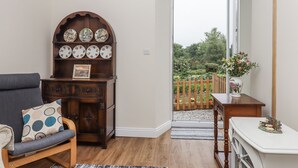 A living room with a wooden cabinet displaying plates, a grey sofa, and a wooden table with a vase. - Aunty Junes Cottage (Okehampton)