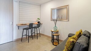 A compact living space with a kitchenette, a dining area with two chairs, a sofa with cushions, a small table with a vase, and a framed picture on the wall. - Charming 1-bedroom apartment near Salento, Finlandia, and Parque Del Cafe (Armenia)