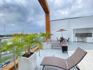 A rooftop terrace with lounge chairs, a table, and an umbrella. There are potted plants and a view of the cityscape. - Charming 1-bedroom apartment near Salento, Finlandia, and Parque Del Cafe (Armenia)