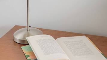 A wooden bedside table with a white lamp, an open book, and a colorful magazine.