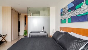 A modern hotel room with a large bed, a desk with a chair, a glass shower enclosure, and a painting on the wall. - Charming 1-bedroom apartment near Salento, Finlandia, and Parque Del Cafe (Armenia)