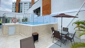 An outdoor swimming pool with a glass enclosure, a seating area with tables and chairs, and a view of surrounding buildings. - Charming 1-bedroom apartment near Salento, Finlandia, and Parque Del Cafe (Armenia)