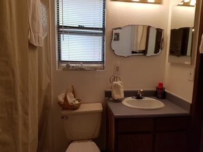 Une salle de bain comprenant des toilettes, un lavabo, un miroir et une fenêtre avec des stores.