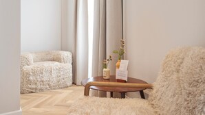 Una habitación acogedora con un sofá beige mullido, una mesa de centro de madera con un jarrón y un menú, y un ventanal con cortinas.