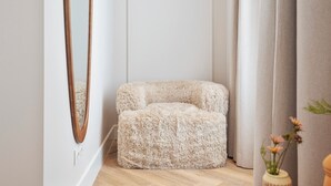 Una habitación con un sofá beige mullido, un espejo grande y un jarrón con flores.