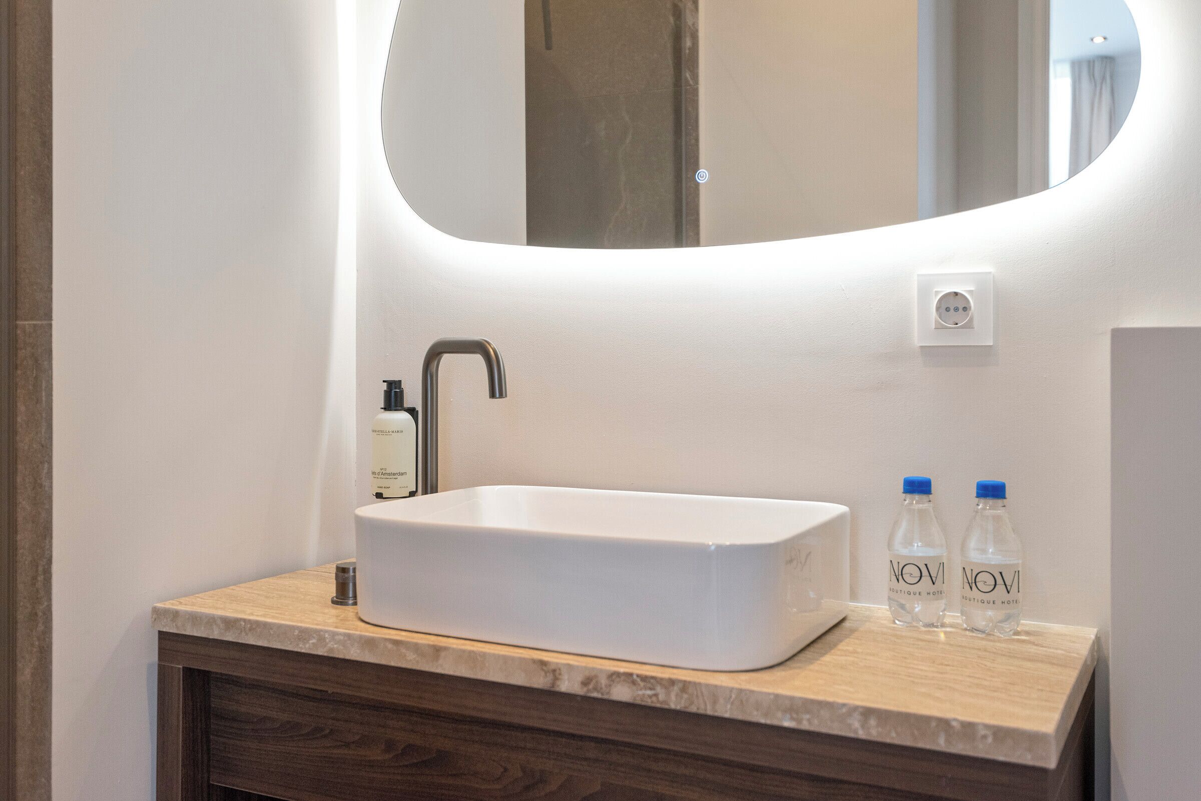 Een moderne badkamer met een rechthoekig wastafel, een spiegel en twee waterflessen op het aanrecht.