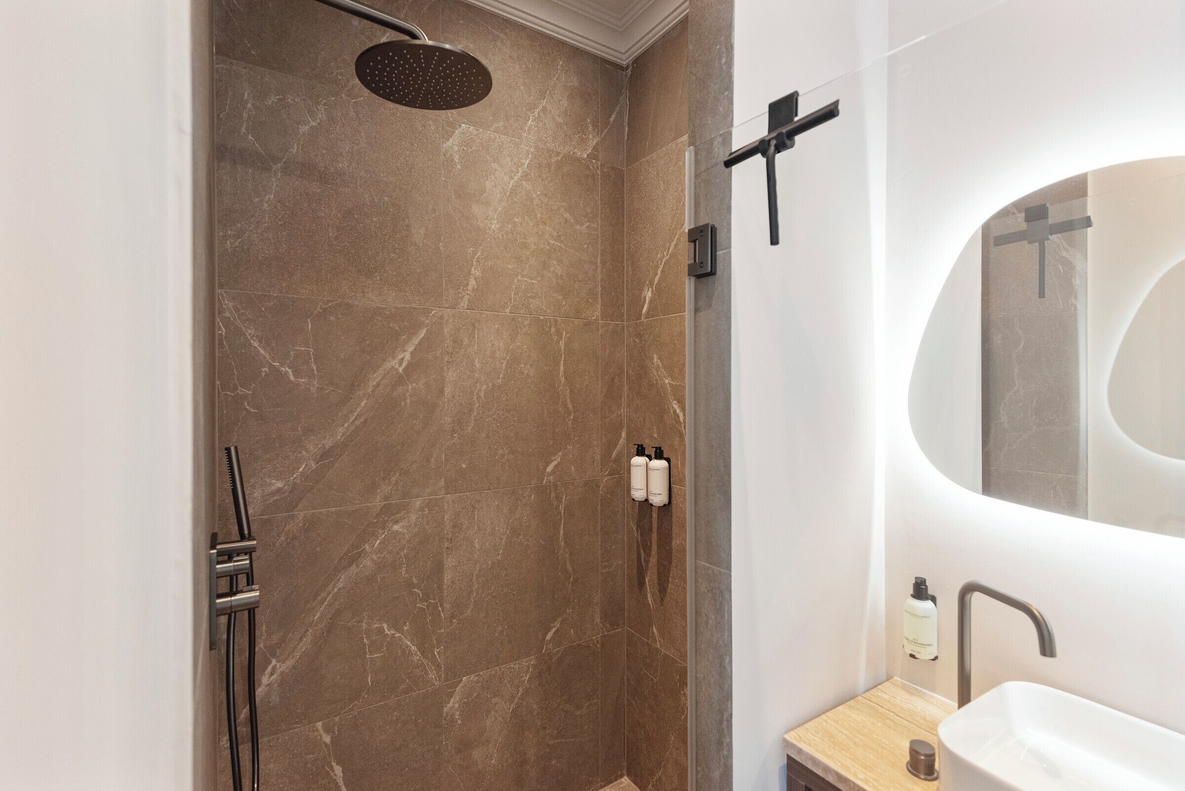 Un baño moderno con ducha de mármol, lavamanos suspendido y un espejo grande.