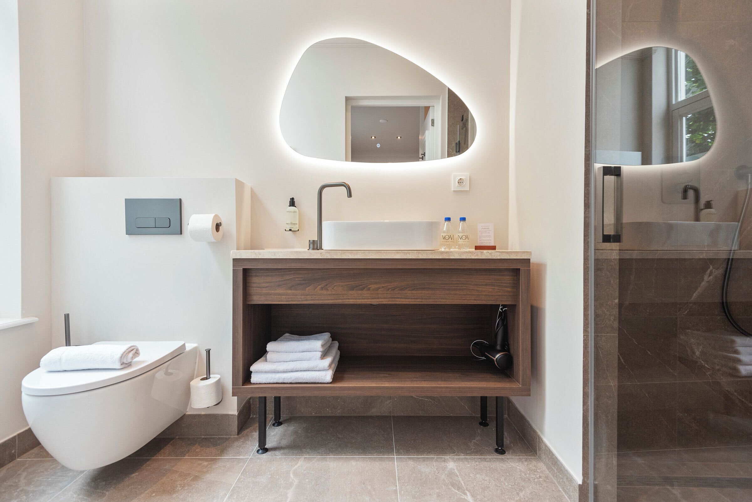 A modern bathroom with a freestanding toilet, a vanity with a mirror, and a shower area.