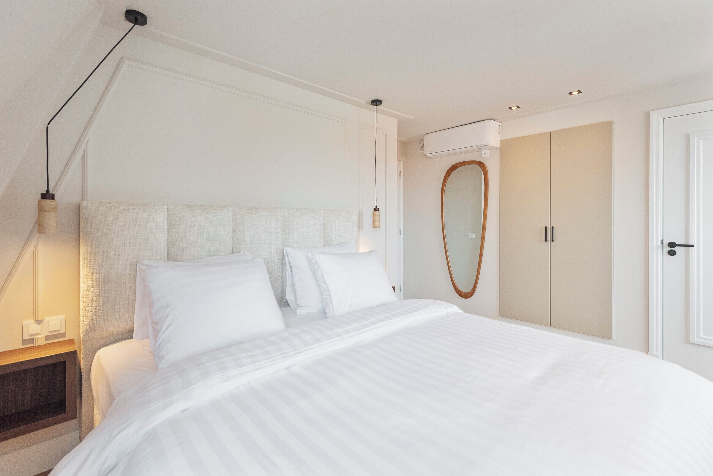 Une chambre à coucher moderne avec un grand lit, une table de chevet, une lampe suspendue et une armoire.