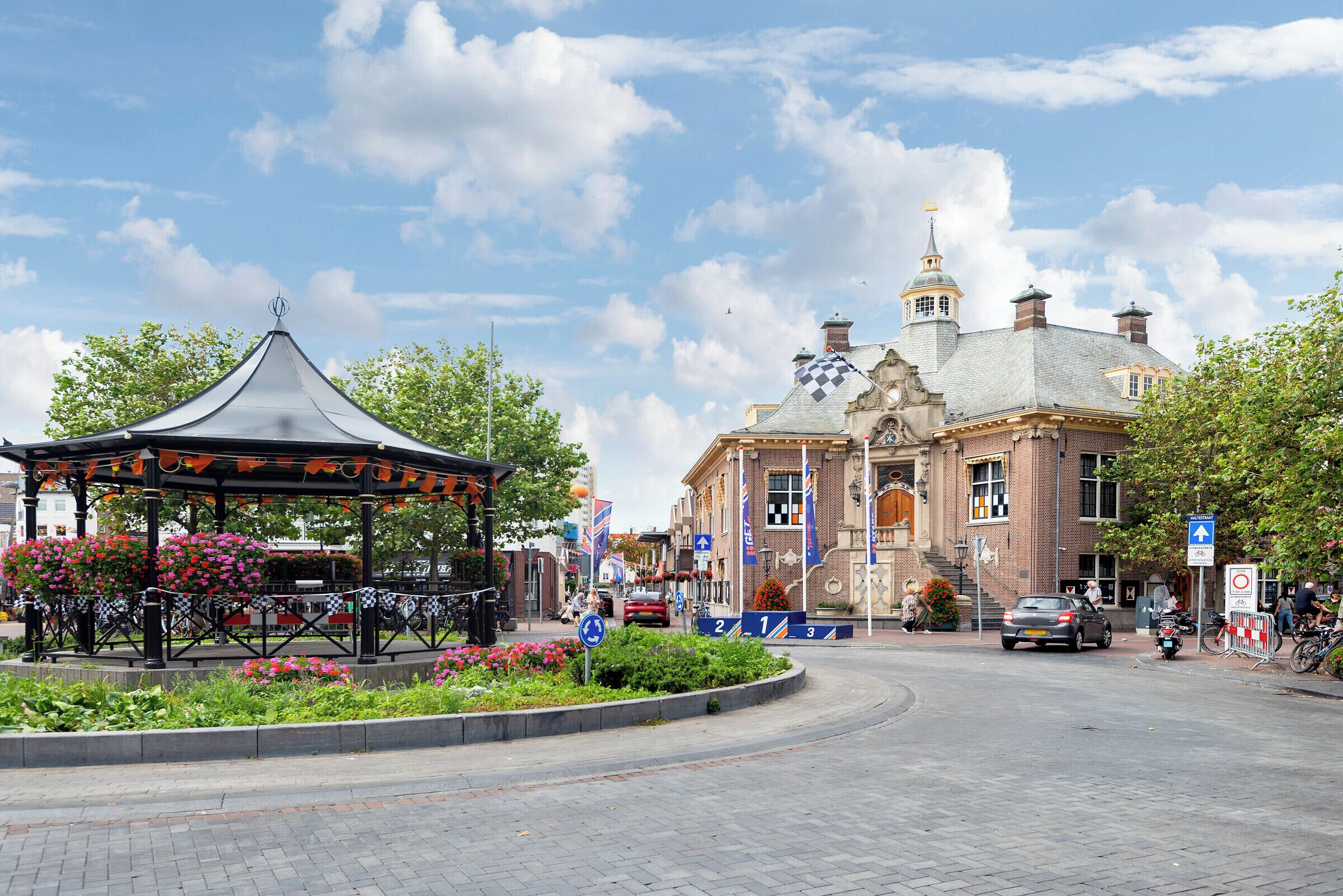A gazebo with flowers, a brick building with a tower, and a clear sky.