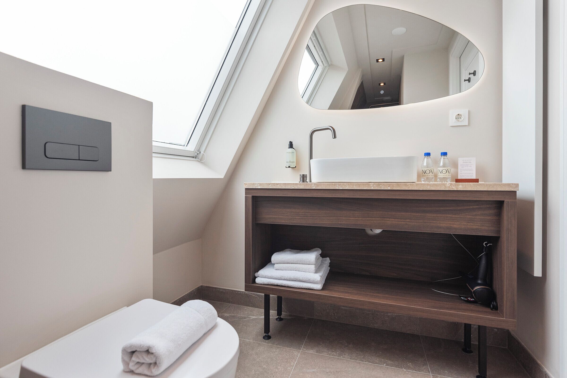 Une salle de bain moderne avec un puits de lumière, un meuble-lavabo avec un miroir et des serviettes soigneusement pliées.