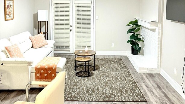 Una sala de estar moderna con un sofá blanco, una mesita redonda, un tapete estampado y una planta grande.