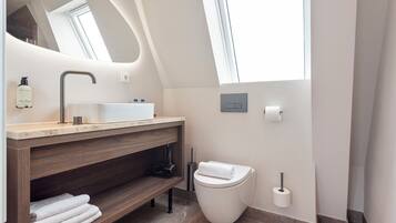A modern bathroom with a skylight, a sink, a toilet, and a towel rack.