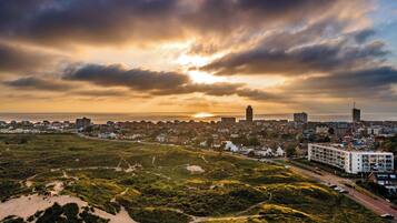 Un paysage urbain côtier, avec un mélange de bâtiments résidentiels et commerciaux, une tour imposante et un coucher de soleil sur l’océan.