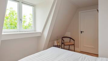 Ein Schlafzimmer mit einem Bett, einem Sessel, einem kleinen Tisch mit einer Vase und einer Tür.