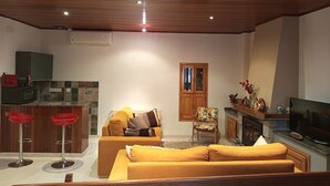 Ein Wohnzimmer mit Holzbalkendecke, einer Couch, einem Fernseher und einer Küchenzeile mit Mikrowelle und Schrank.