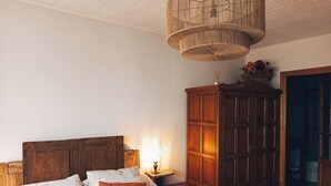 Ein Schlafzimmer mit hölzerner Kopfteil, einem Bett mit weißen und orangefarbenen Kissen, einem Holzschrank und einer Pendelleuchte.