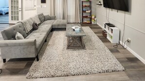 Una sala de estar moderna con un sofá seccional, una mesa de centro, un televisor montado en la pared y una estantería.