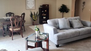 A living room with a gray sofa, a dining table with chairs, a glass coffee table, and a potted plant.