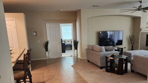 A spacious living room with a large flat-screen TV, a sofa, and a dining area with chairs.
