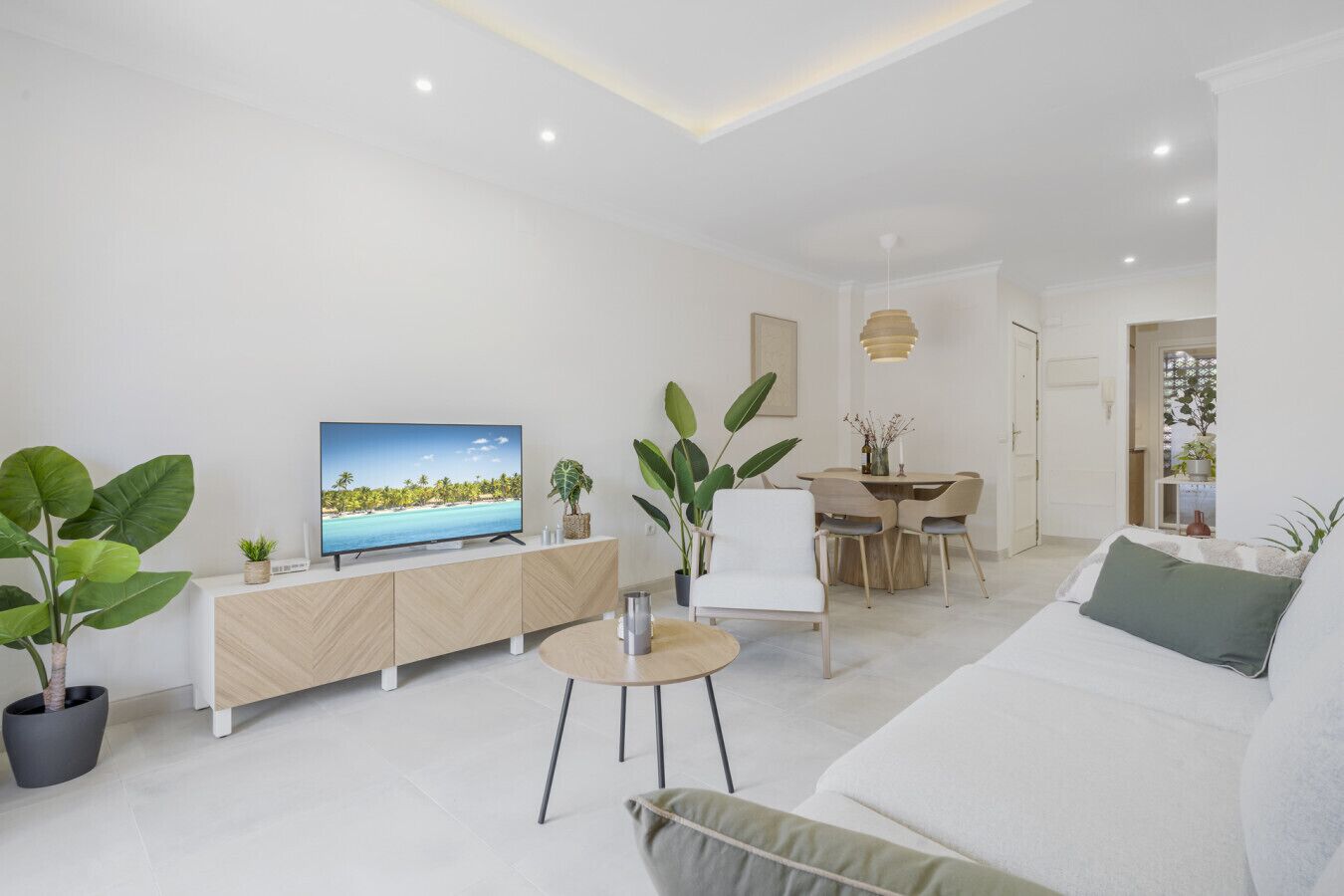 A modern living room with a flat-screen TV, a dining area, and a sofa.