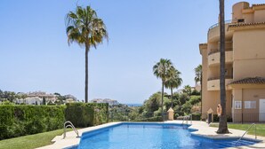 Piscina con vista despejada al mar, rodeada de palmeras y un edificio con balcones.