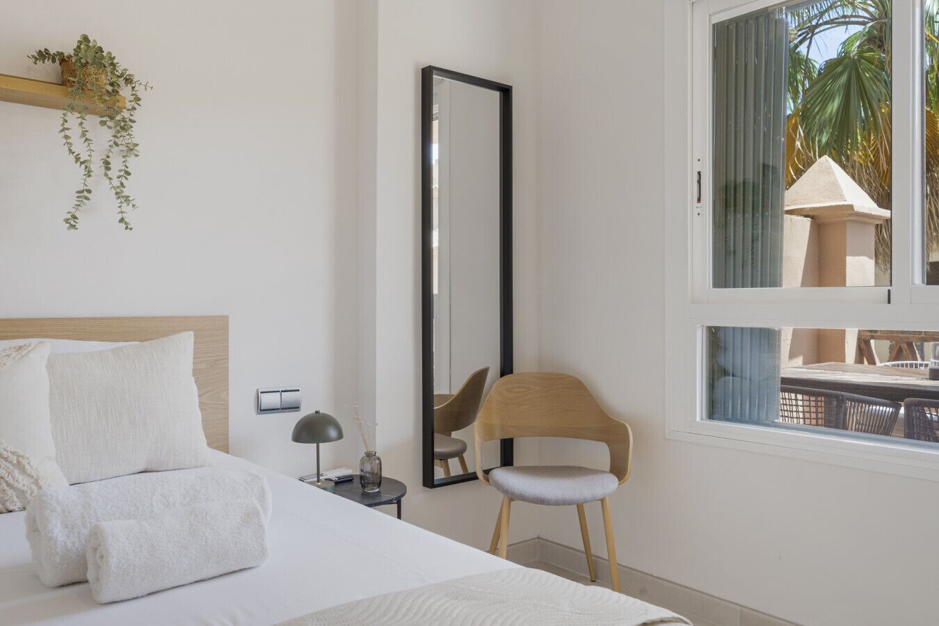 Hotellihuone, jossa on sänky, tuoli, peili ja ikkuna, josta avautuu näkymä palmuille.