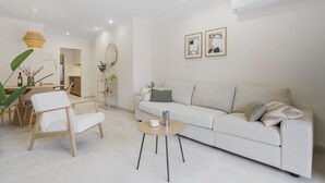 Una sala de estar moderna con un sofá blanco, una mesa de centro y una zona de comedor con una mesa y sillas de madera.