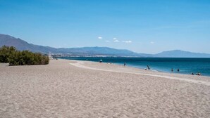 Una playa con cielo despejado, montañas al fondo y algunas personas disfrutando el agua.