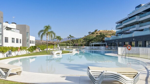 A swimming pool with lounge chairs, a lifebuoy, and a view of a hill with buildings. - Luxury 3 BR apartment with terrace, pool & gym (La cala de mijas)