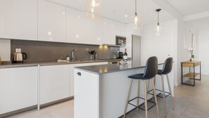 A modern kitchen with white cabinets, stainless steel appliances, and a central island with bar stools. - Luxury 3 BR apartment with terrace, pool & gym (La cala de mijas)