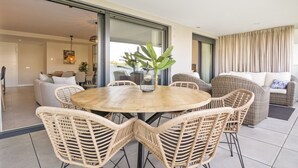A modern living room with a round wooden table, wicker chairs, and a large window with curtains. - Luxury 3 BR apartment with terrace, pool & gym (La cala de mijas)