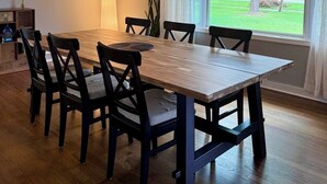 Un comedor con una mesa y sillas de madera, una lámpara colgante y vistas a un paisaje verde a través de un ventanal amplio.